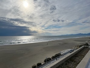 A coastal view with a beach, a road parallel to the shore, and distant mountains.