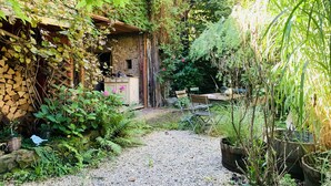 A rustic outdoor area with a gravel path, wooden furniture, and potted plants.