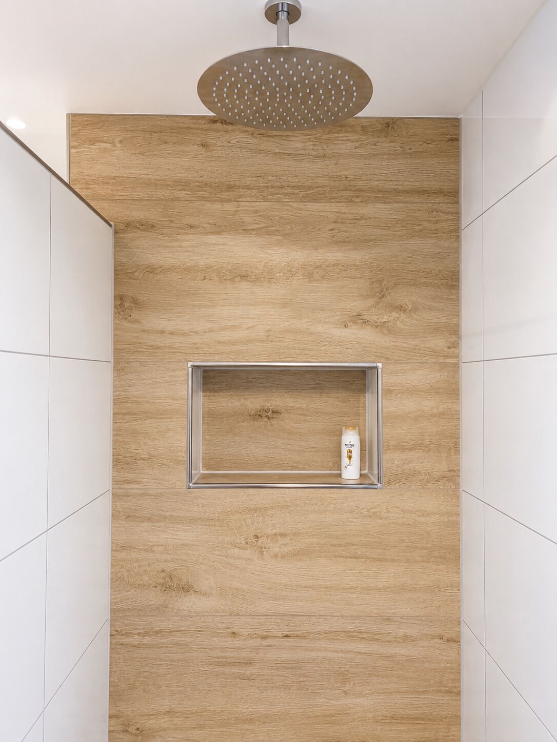 A shower with a wooden panel wall, a built-in shelf, and a ceiling-mounted showerhead.