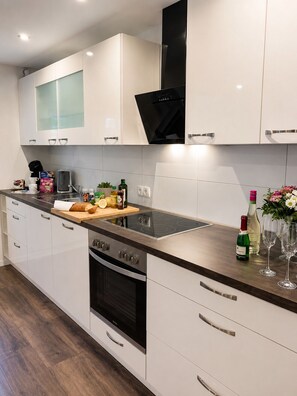A modern kitchen with white cabinets, a black range hood, a stainless steel oven, and a wooden countertop with various items.