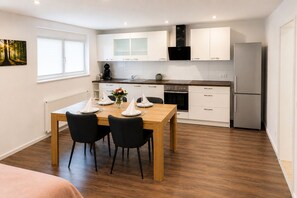 Eine moderne Küche mit weißen Schränken, einem Edelstahl-Kühlschrank und einem Essbereich mit Holztisch und schwarzen Stühlen.