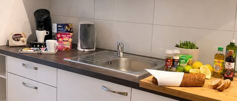 A modern kitchen with white cabinets, a stainless steel sink, and various food items on the counter.