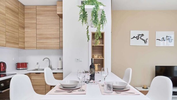 A modern kitchen with white cabinets, a dining table set for four, and a TV in the background.