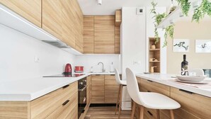 A modern kitchen with wooden cabinets, white countertops, a built-in oven, and a bar area with stools. - Stylish Apartment with Balcony | Private Parking (Wroclaw)