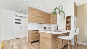 A modern kitchen with wooden cabinets, a central island, white chairs, and a hanging plant. - Stylish Apartment with Balcony | Private Parking (Wroclaw)