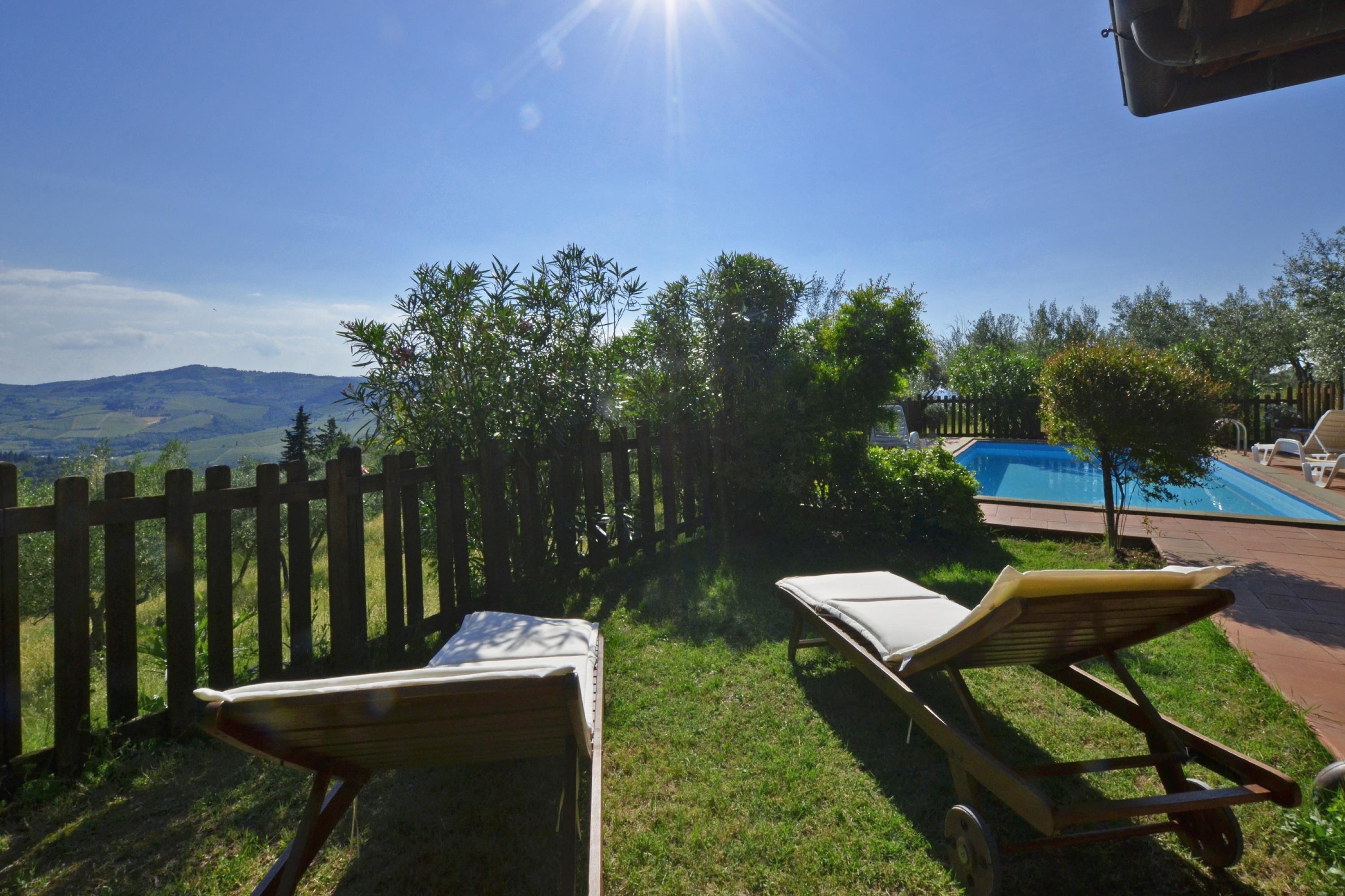 A backyard with a wooden fence, a pool, and two sun loungers.