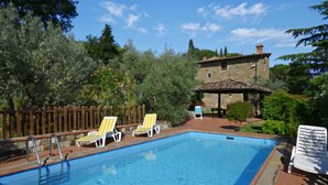 A swimming pool with lounge chairs, a stone building, and a wooden fence in the background. - Casa Citille (Greve in Chianti)