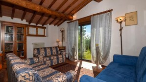 A living room with a sofa, a blue armchair, a wooden ceiling, and a window with curtains. - Casa Citille (Greve in Chianti)