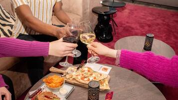 Un grupo de personas brindando con copas de vino alrededor de una mesa redonda con pizza, aperitivos y un menú.