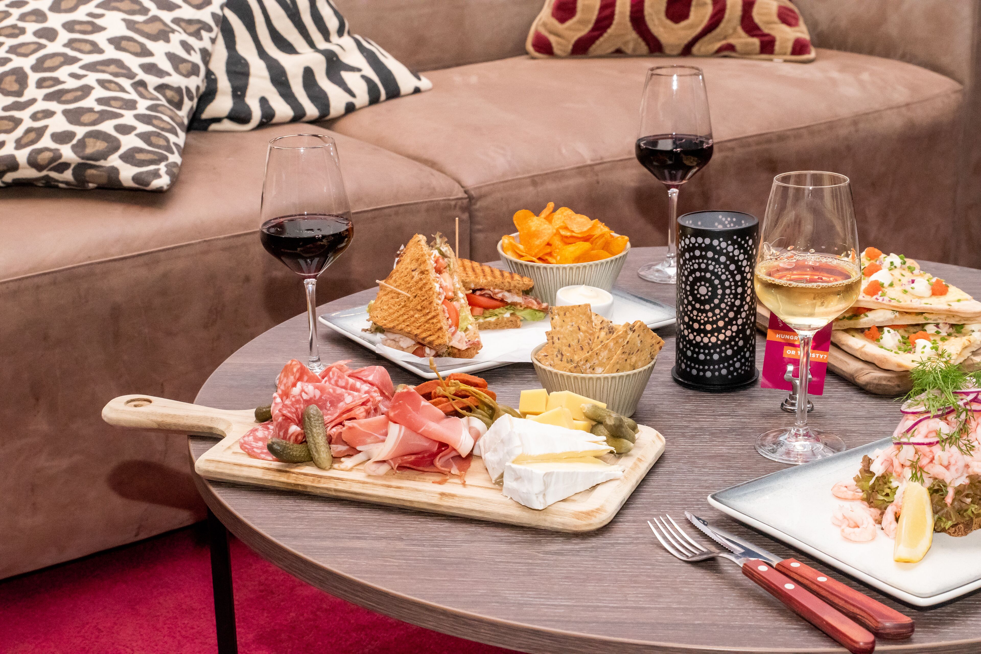 Una mesa redonda con diversos alimentos, como sándwiches, papas fritas y queso, junto con copas de vino.