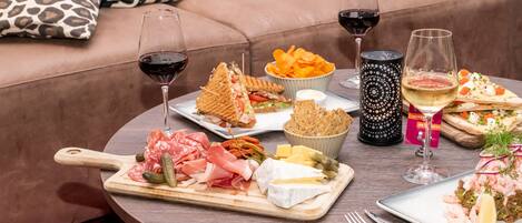Una mesa redonda con diversos alimentos, como sándwiches, papas fritas y queso, junto con copas de vino.
