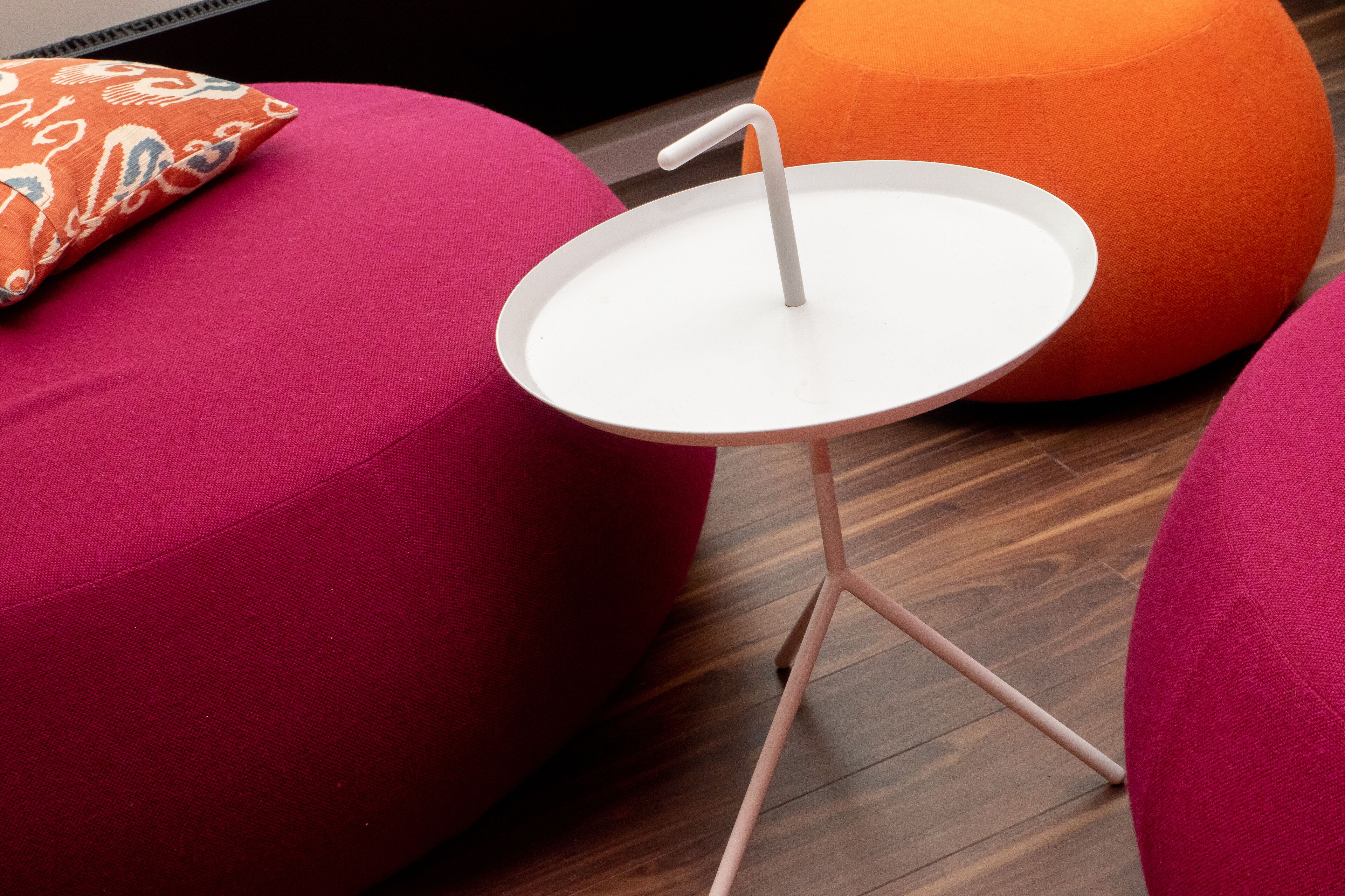 Een moderne kamer met een ronde witte tafel, een roze bank en een oranje poef.