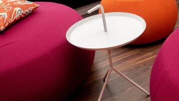 Een moderne kamer met een ronde witte tafel, een roze bank en een oranje poef.