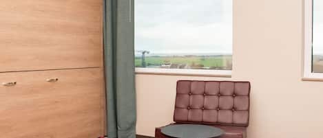 A room with a wooden wardrobe, a brown leather chair, a small round table, and a colorful hexagonal patterned carpet.