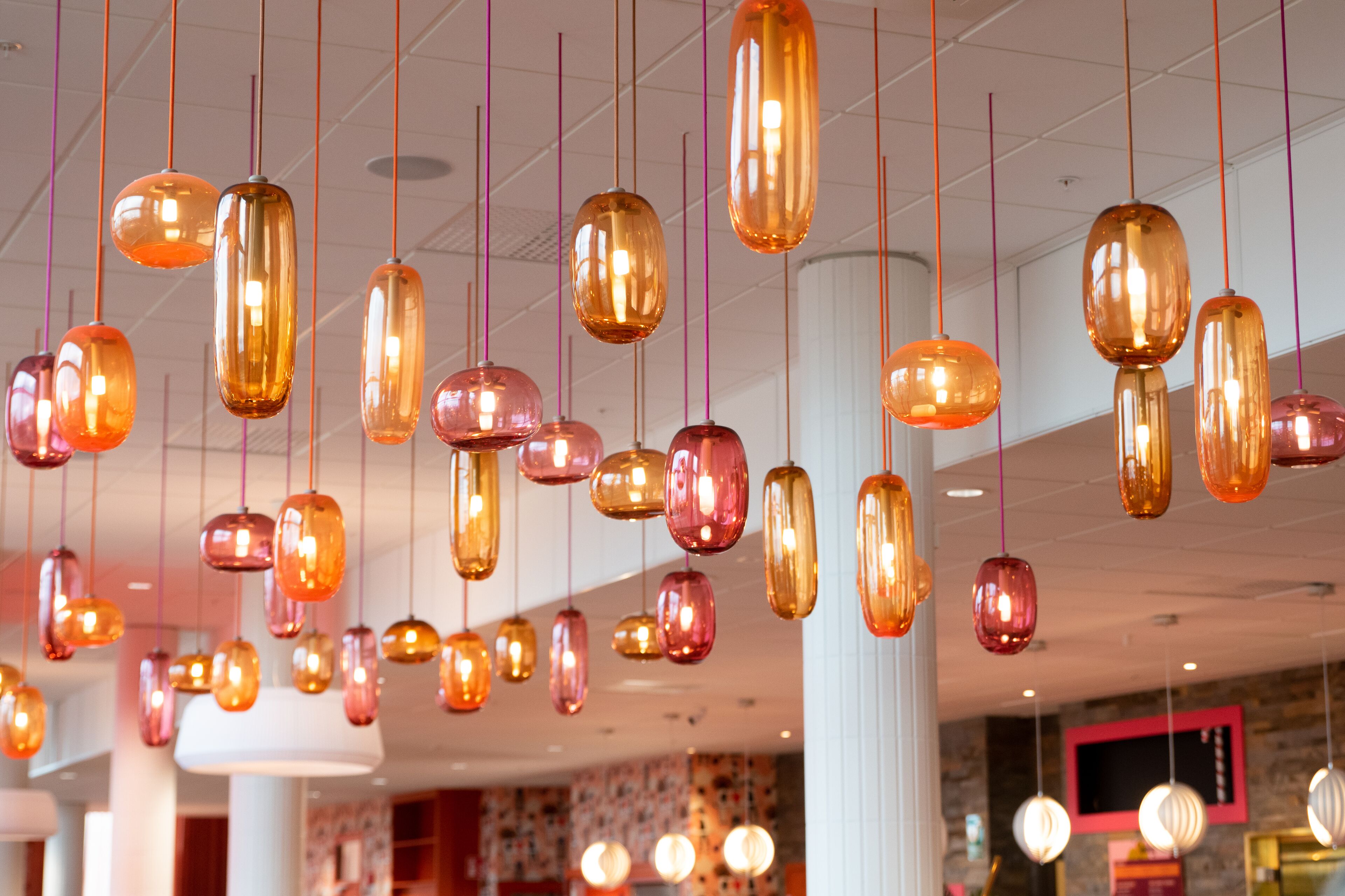 A hotel interior with multiple hanging pendant lights and a visible television screen on the wall.