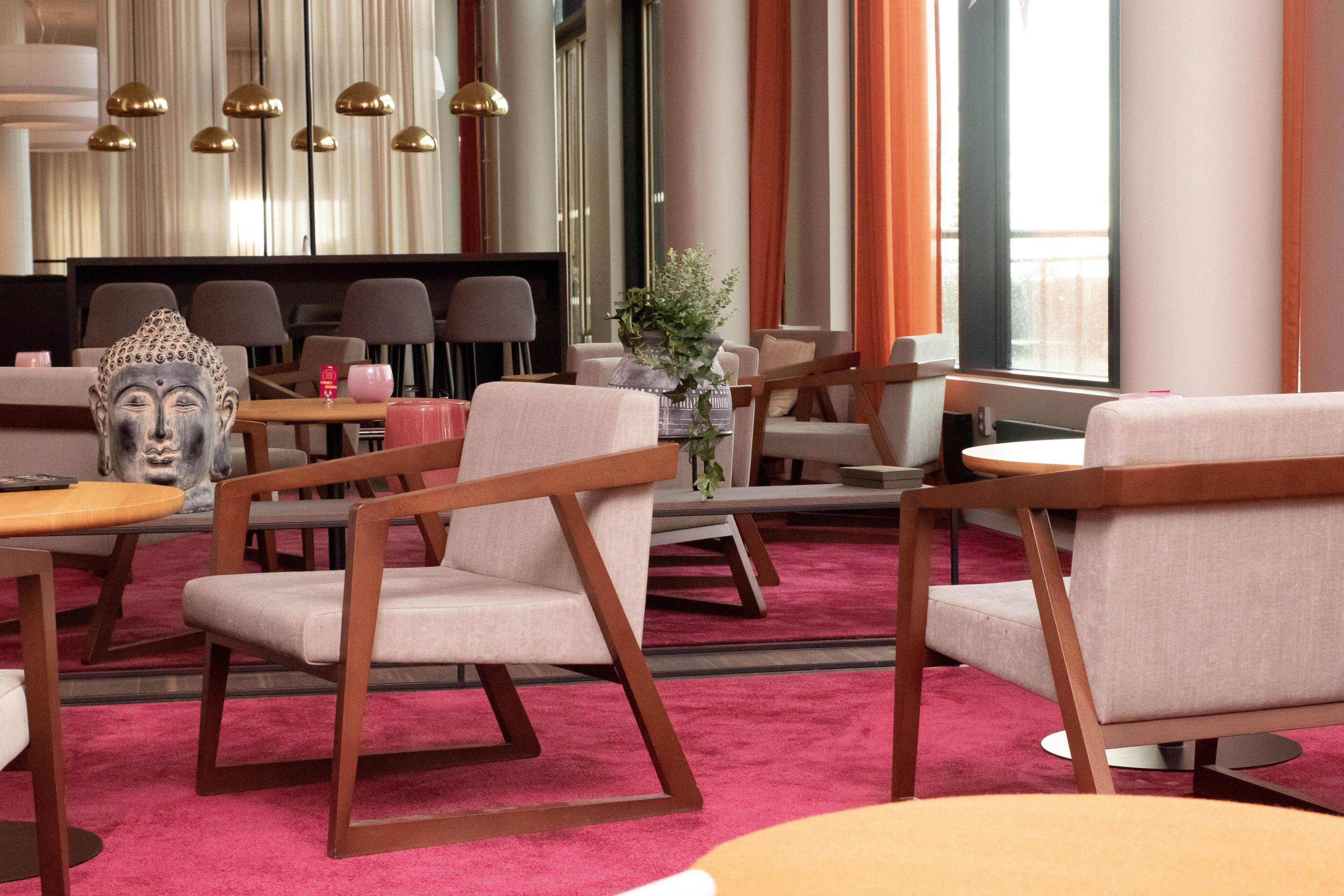 Een moderne hotellobby met houten stoelen, een Boeddhabeeld en een rode loper.