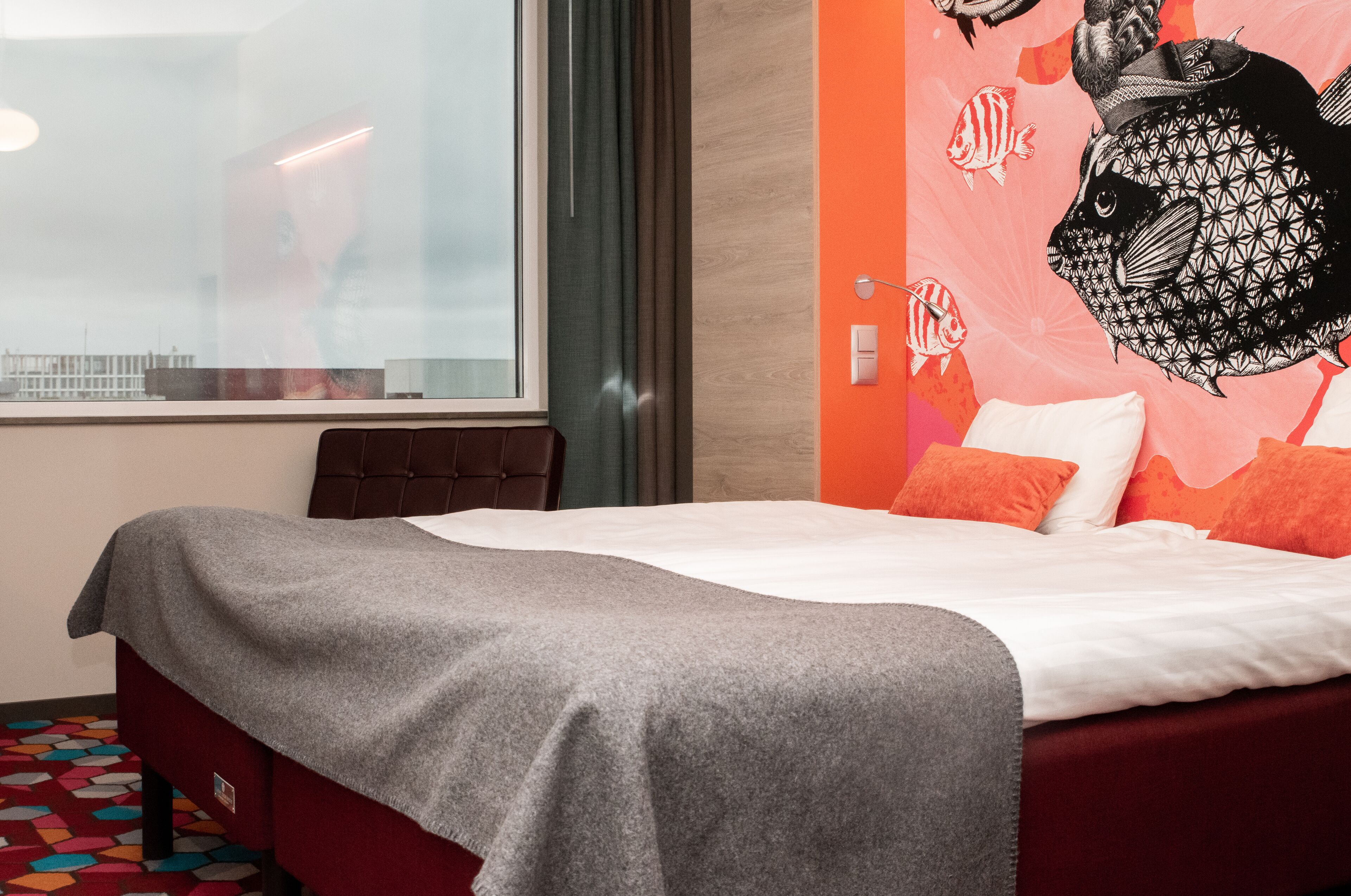 A hotel room with a bed, a large window, and a wall mural.