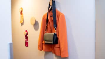 En vägg med en upphängd orange kavaj, en svart och grå handväska och en röd etikett med texten ”Stör inte”.