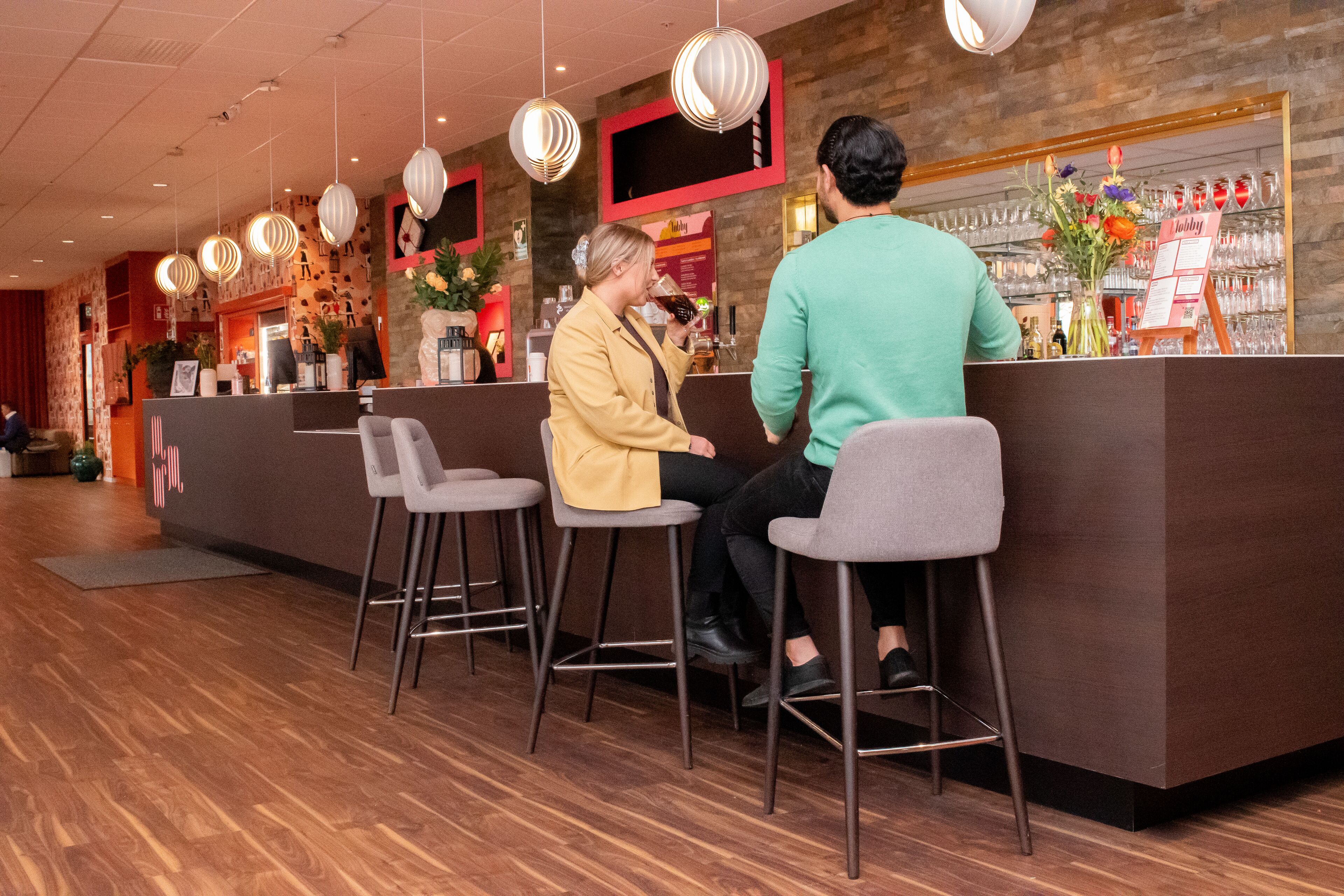 Zona de bar con mostrador de recepción, taburetes, lámparas colgantes y una estantería para vinos.