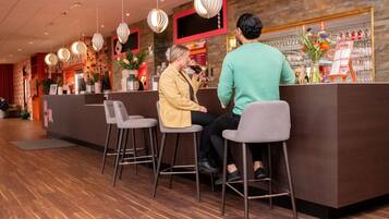 Zona de bar con mostrador de recepción, taburetes, lámparas colgantes y una estantería para vinos.