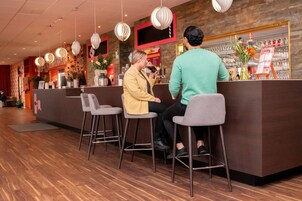 Zona de bar con mostrador de recepción, taburetes, lámparas colgantes y una estantería para vinos.