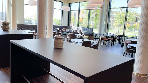 Un espace intérieur spacieux, doté de nombreuses tables et chaises, de grandes fenêtres et d’un éclairage moderne suspendu.