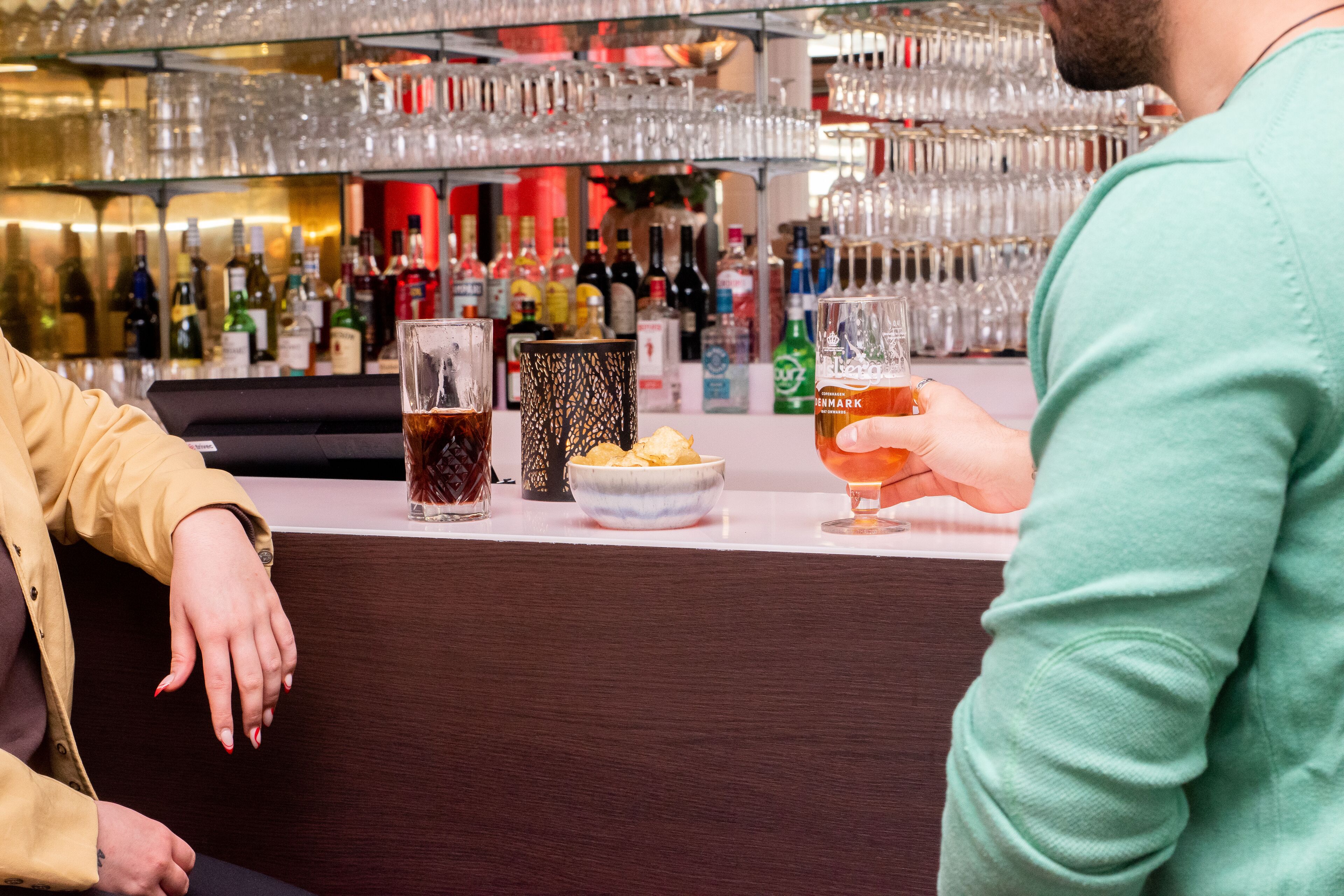 A bar area with a counter, glasses, bottles, and a bowl of snacks.