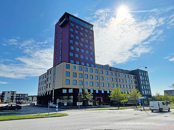 A multi-story building with a mix of glass and brick facades, a parking sign, and a van parked in front. - Motel L Lund (Lund)