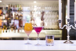 A bar area with two cocktails, a candle holder, and a container of nuts.