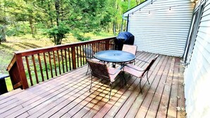 A wooden deck with a table and chairs, surrounded by a railing, overlooking a forested area. - Mountain gateway in the beautiful Lake Harmony (lake harmony)