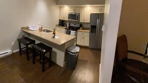 A modern kitchen with a central island, stainless steel appliances, and a small dining area with a chair. - Mountain gateway in the beautiful Lake Harmony (lake harmony)