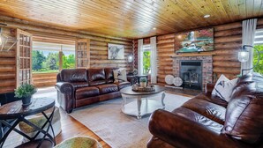 A log cabin interior with a leather sofa, a fireplace, and a large window. - Private Log Estate by Winery | Trails & Fire Pit (Kingsville)