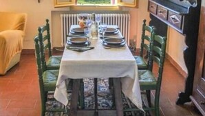 A dining area with a table set for four, chairs, a view through an open window, a radiator, and a shelf with items. - La Torre di Rua (SAN PIETRO DI FELETTO)