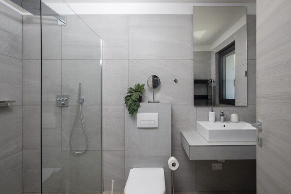 Une salle de bain moderne avec une douche à parois de verre, des toilettes, un lavabo et un miroir.