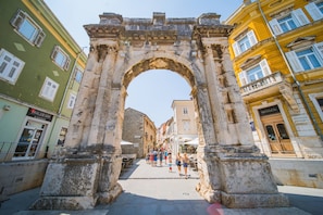 An ancient stone archway in a city square with people walking through it.