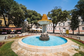 A fountain with a tiered design in a public square surrounded by trees and buildings.