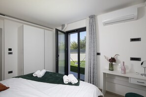 A modern bedroom with a bed, a desk, a bathroom, and a view of the outdoors.