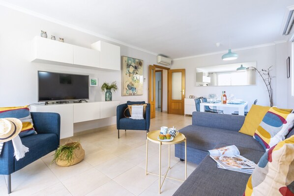 Ein modernes Wohnzimmer mit einer Couch, Sesseln, einem Couchtisch und einem Fernseher.