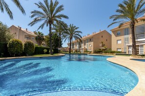 Ein Swimmingpool, umgeben von Palmen und sandfarbenen Gebäuden mit Balkonen.