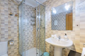 Ein Badezimmer mit einer Duschkabine, einem Waschbecken mit Spiegel und einer gefliesten Wand mit Rautenmuster.