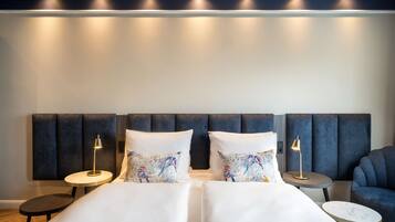 Habitación de hotel con una cama grande, dos mesitas de noche con lámparas, una mesita redonda pequeña y un sillón azul.