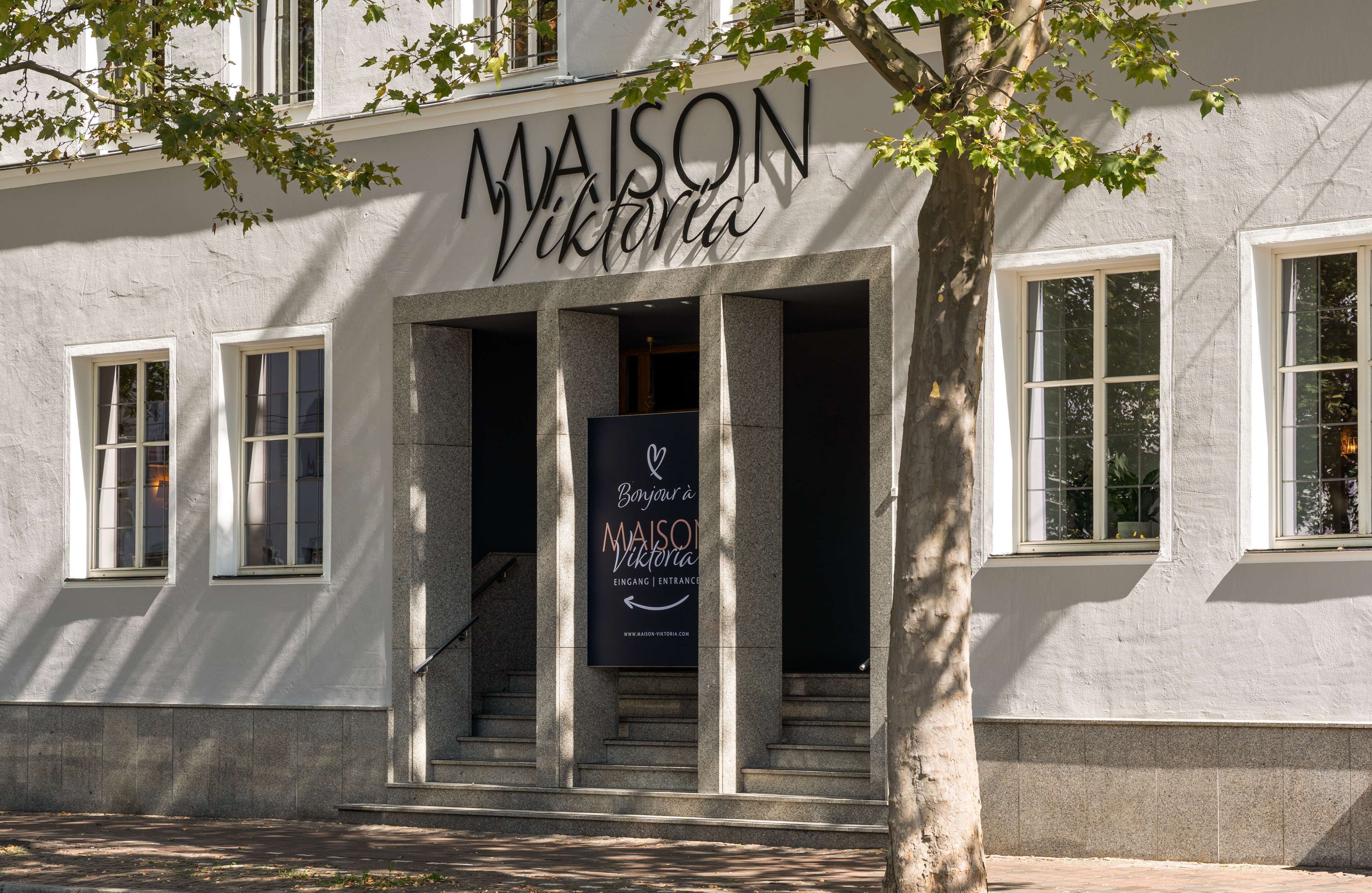 Un edificio con el letrero "MAISON Victoria" y un cartel que dice "Banyou & MAISON Victoria EINGANG & ENTRANCE".