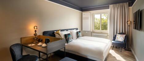 A modern hotel room with a large bed, a desk, a chair, and a small table.