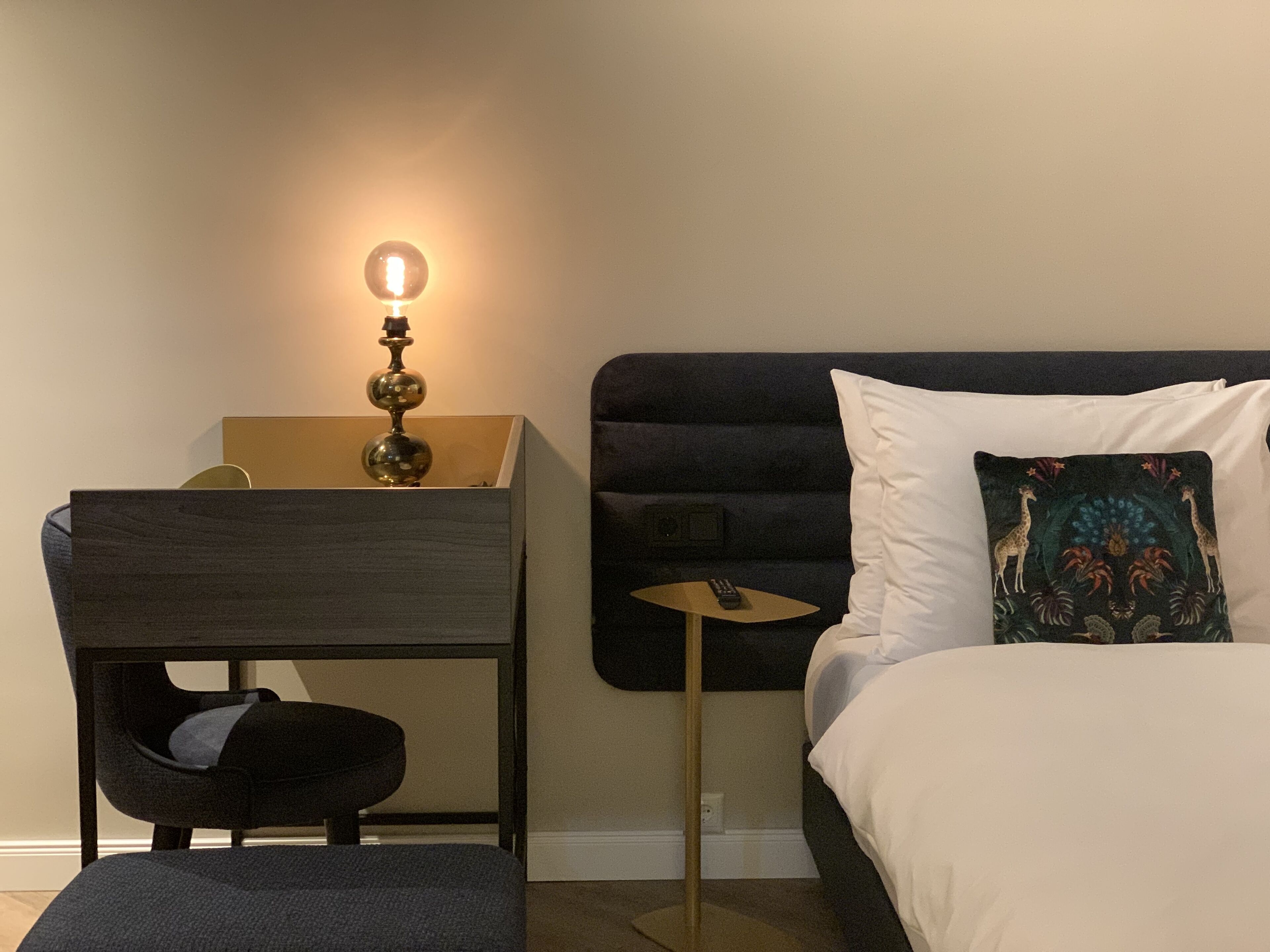 Un dormitorio con cama, escritorio, silla y mesita de noche con lámpara.