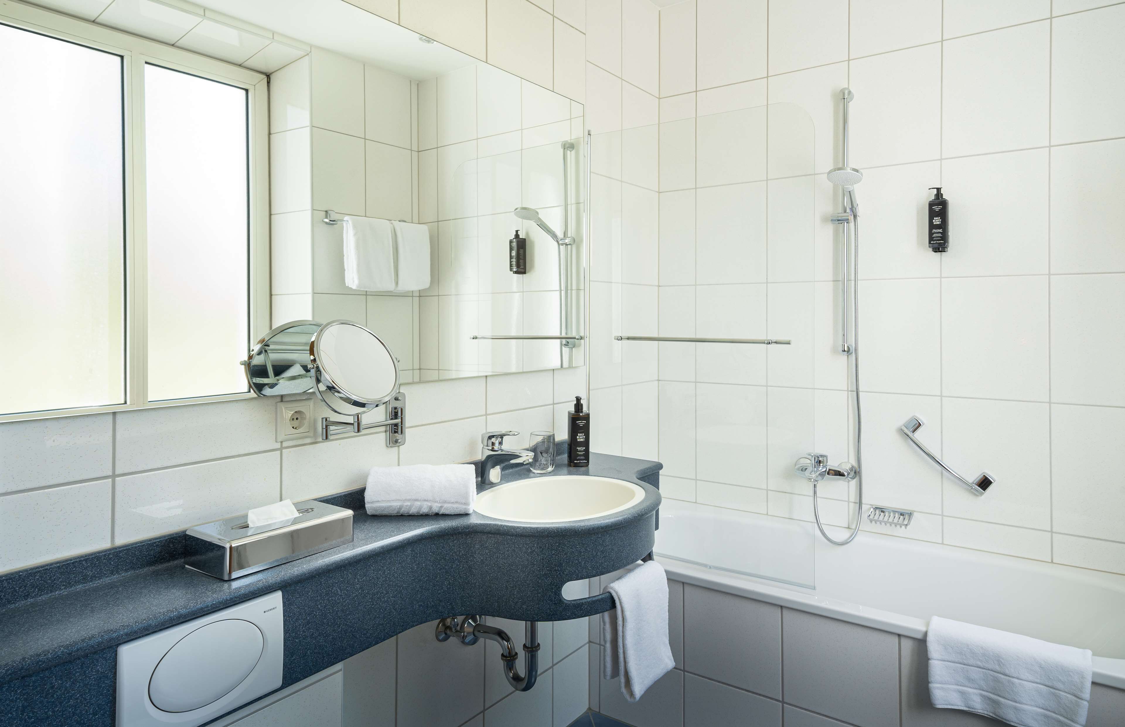 Ein modernes Badezimmer mit einem großen Spiegel, einem Waschbecken mit Handtuch, einer Dusche und einer Toilette.
