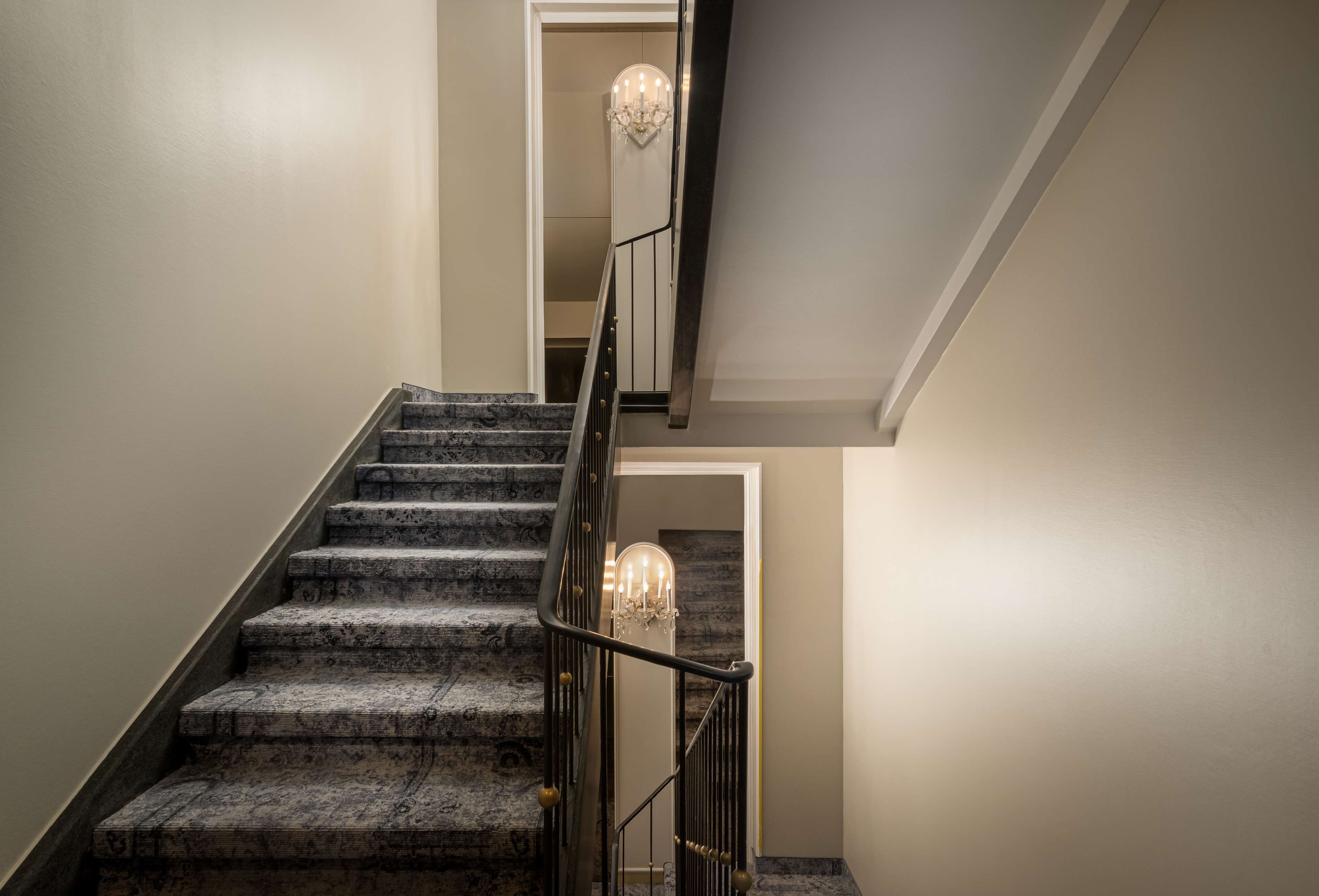 A staircase with a dark metal railing and a chandelier at the top.