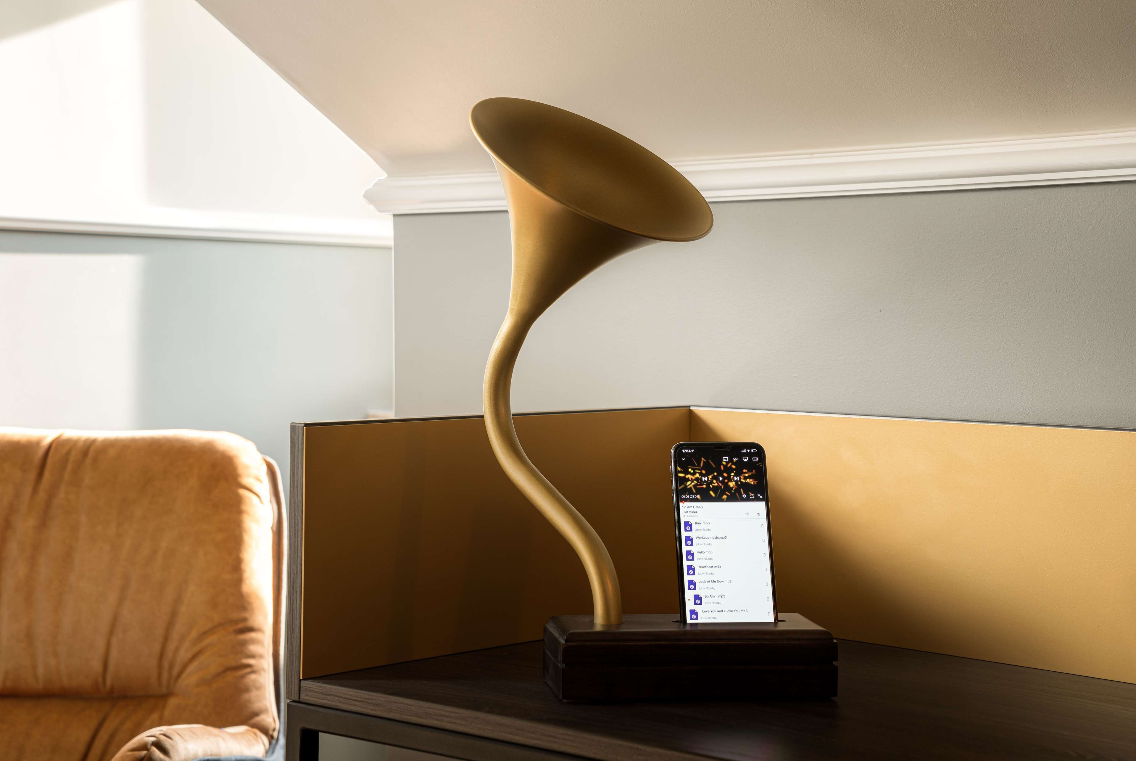 Une lampe moderne au design incurvé, posée sur une table de chevet, à côté d’un smartphone affichant une liste.