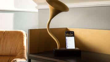 Une lampe moderne au design incurvé, posée sur une table de chevet, à côté d’un smartphone affichant une liste.