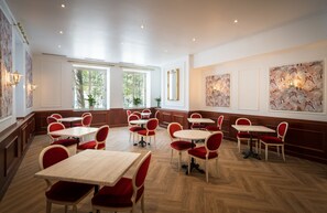 Ein Restaurantinnenraum mit Holzböden, roten Stoffstühlen und weißen Tischen.