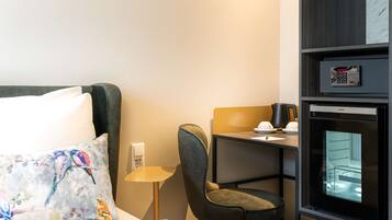 A hotel room with a bed, a desk, a chair, a minibar, and a built-in oven.